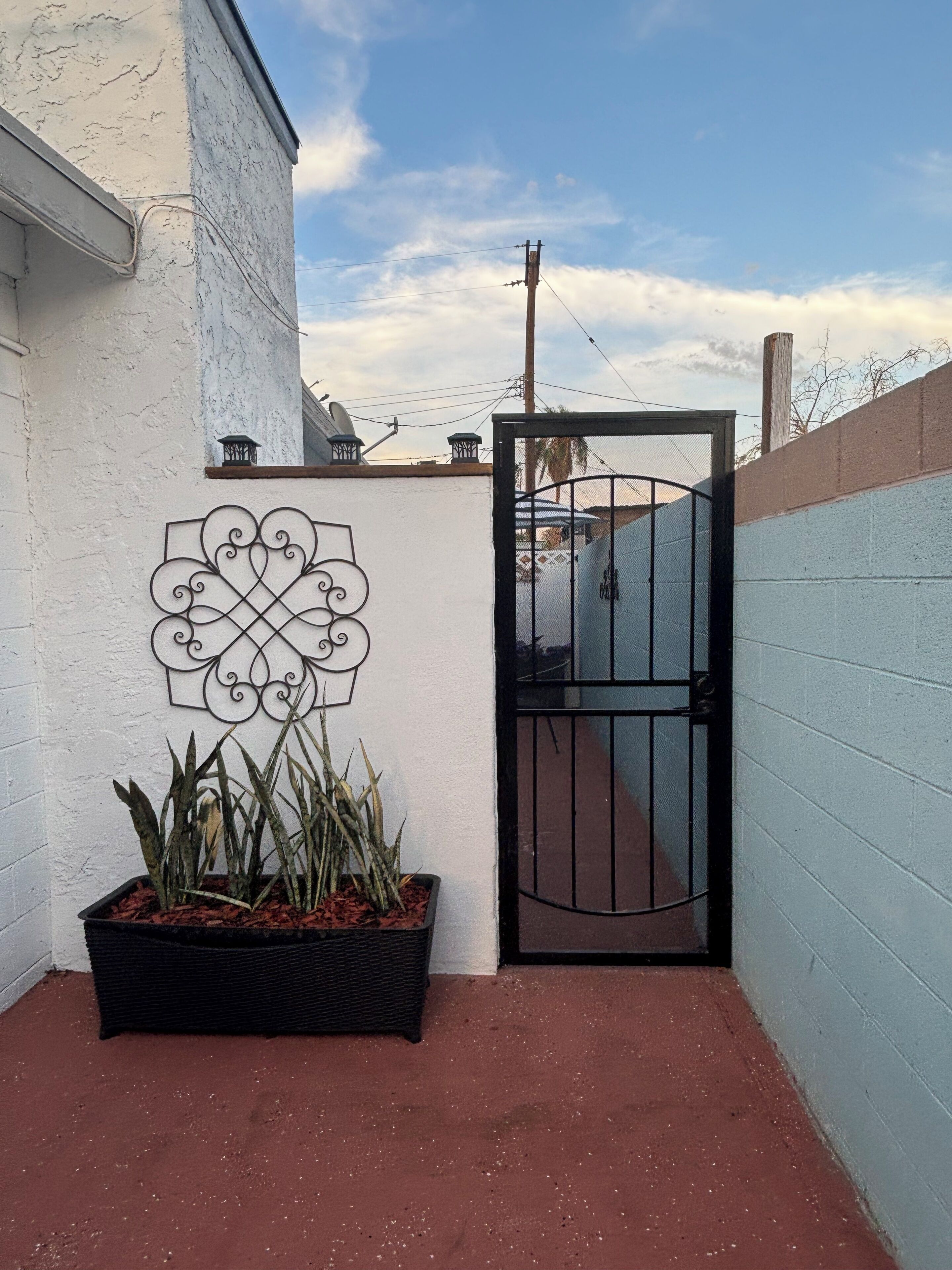 Una entrada protegida con un cartel de metal decorativo, una planta en maceta y un cielo despejado.