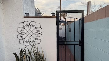 Una entrada protegida con un cartel de metal decorativo, una planta en maceta y un cielo despejado.