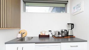 Een moderne keuken met een ingebouwd spoelbakje, witte keukenkastjes, een raam en diverse apparaten, waaronder een broodrooster en een koffiezetapparaat.