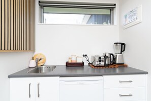 A modern kitchen with a built-in sink, white cabinets, a window, and various appliances including a toaster and a coffee maker. - 🥭 Mango Manor: Relaxing, private group getaway (Raglan)