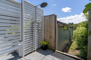 Eine Terrasse mit weißem Zaun, einem Holztor, einem Blumentopf und einem kleinen Schuppen.