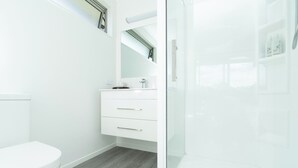 Een moderne badkamer met een wit toilet, een wastafel met lades en een douchecabine met glazen wanden.