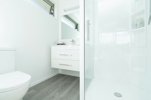 A modern bathroom with a white toilet, a vanity with drawers, and a glass shower enclosure. - 🥭 Mango Manor: Relaxing, private group getaway (Raglan)