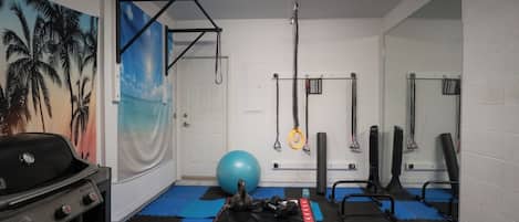 A home gym with exercise equipment, a blue mat, and a wall with a palm tree mural.