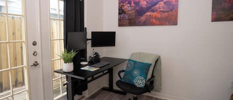 Una oficina en casa con escritorio, computadora, silla y una ventana con cortinas.