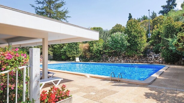 A rectangular swimming pool with a stone wall and a covered area with chairs. - Upstays Cosy Studio 15m² with pool and quiet (Cannes)