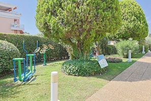 Un jardín cuidado con equipo de ejercicio, un árbol grande y un sendero.