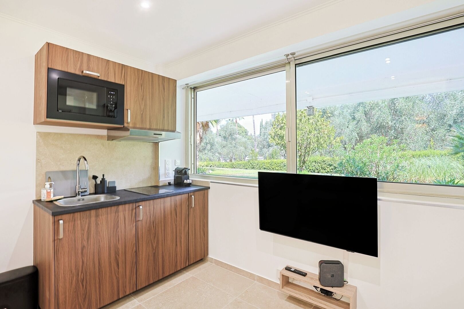 A modern kitchen with a built-in microwave, a sink, and a window with a view of greenery.
