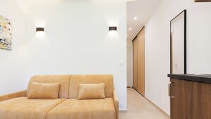 A modern living room with a sofa, a wooden cabinet, and recessed ceiling lighting. - Upstays Cosy Studio 15m² with pool and quiet (Cannes)
