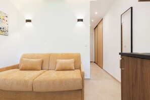 A modern living room with a sofa, a wooden cabinet, and recessed ceiling lighting. - Upstays Cosy Studio 15m² with pool and quiet (Cannes)