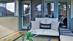 Ein überdachter Patio-Bereich mit einer Couch, Kissen und einem Blumentopf.