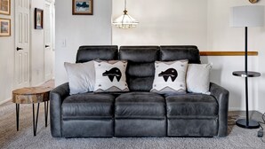 Ein schwarzes Ledersofa mit zwei gemusterten Kissen, einer Pendelleuchte und einem kleinen Holztisch.