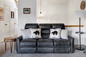 A black leather sofa with two patterned pillows, a hanging light fixture, and a small wooden table. - 2BR/2.5BA Bear Meadows Condo on Golf Course (Big Bear Lake)