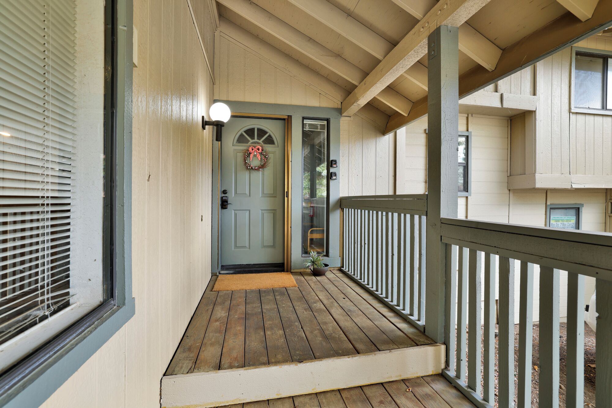 A wooden porch with a door, a light fixture, and a railing.