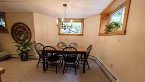A dining area with a wooden table and chairs, a chandelier, a window with plants, and a woven wall decoration. - Mountains, golfing, hiking, tram and waterpark! (Jay)
