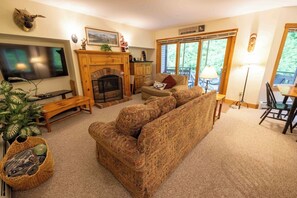 A cozy living room with a fireplace, a sofa, a television, and a dining area with natural light. - 4 bdrms, golf, hikes, tram and waterpark! (Jay)