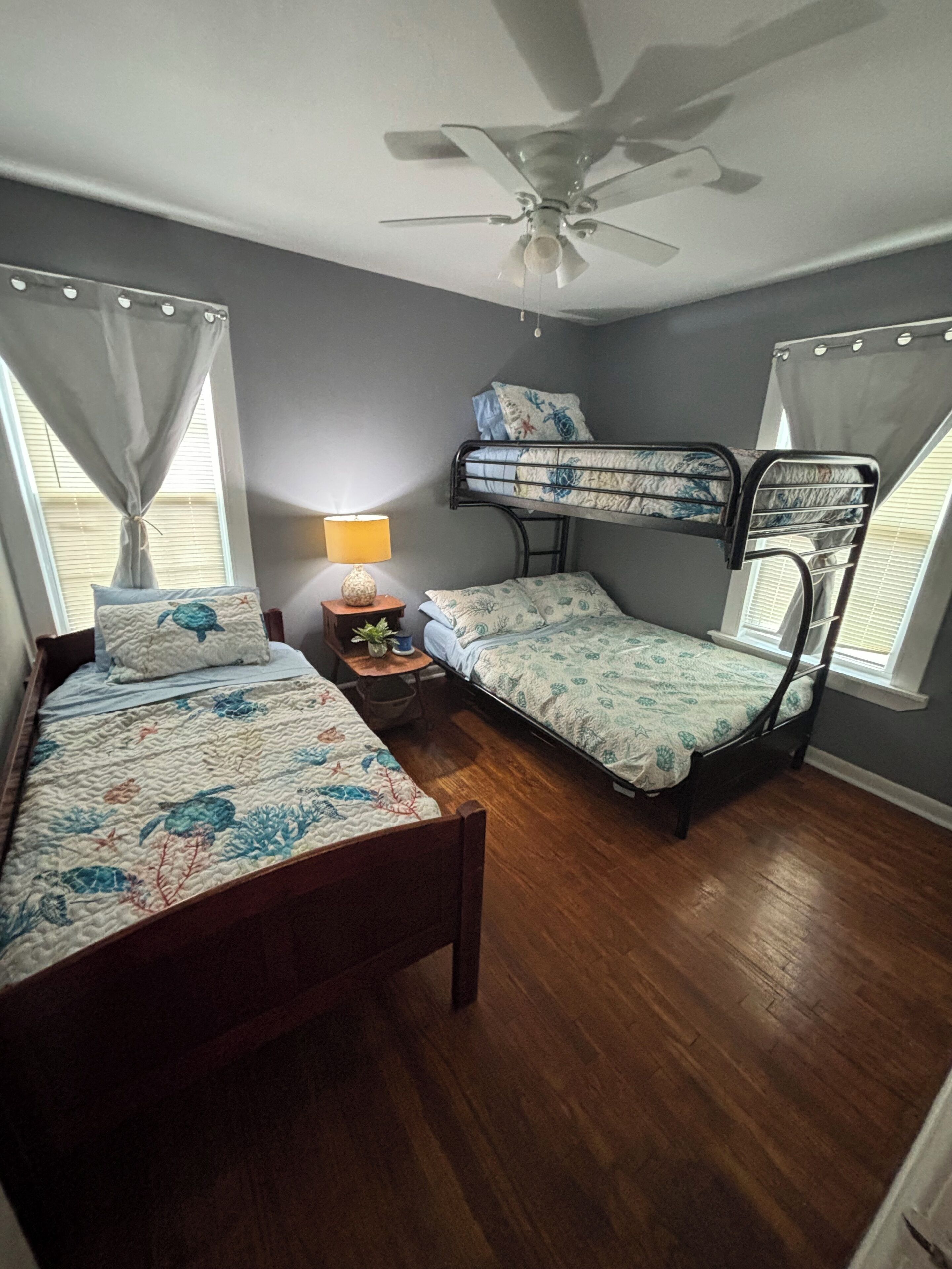 Un dormitorio con una cama individual, una cama litera, un ventilador de techo y una mesita de noche con una lámpara.