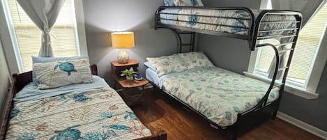 Un dormitorio con una cama individual, una cama litera, un ventilador de techo y una mesita de noche con una lámpara.