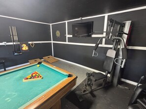 Ein Billardtisch mit Kugeln und Spielstöcken, eine Dartscheibe und ein an der Wand befestigter Fernseher.