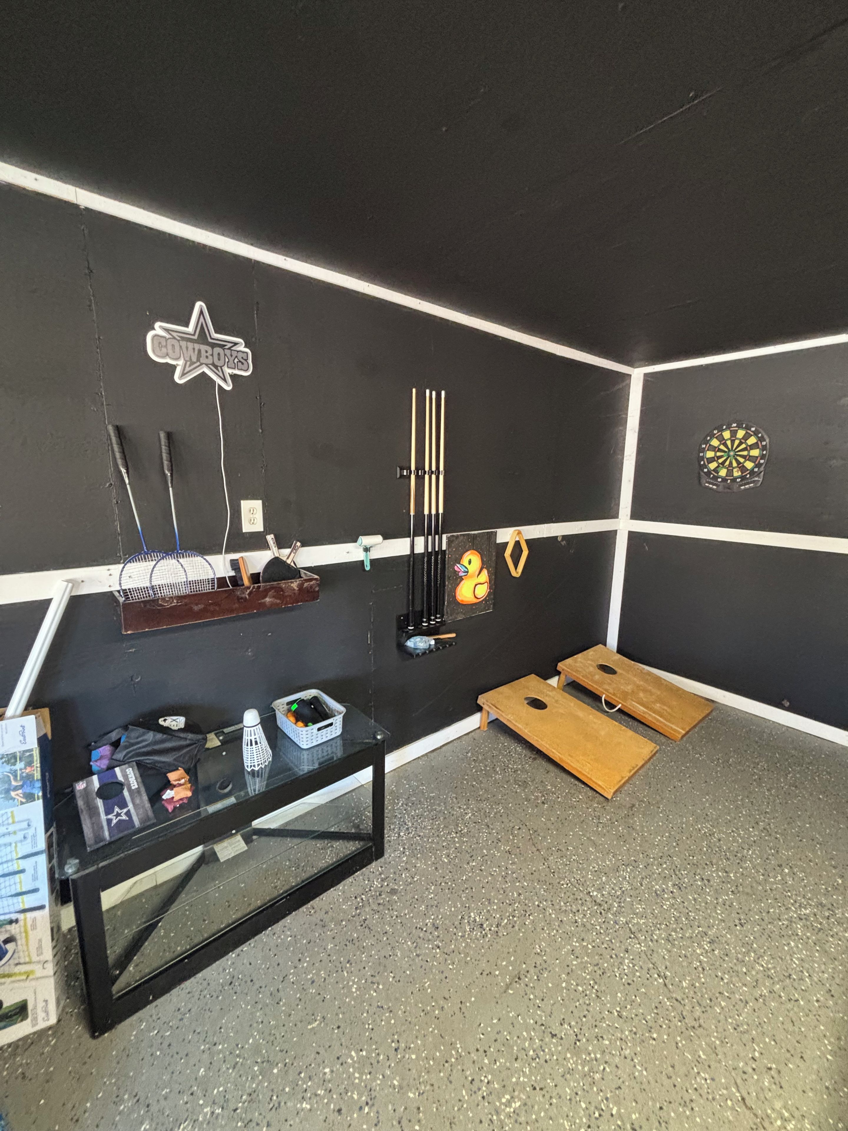 A room with a dartboard, a table with various items, and a small wooden platform.