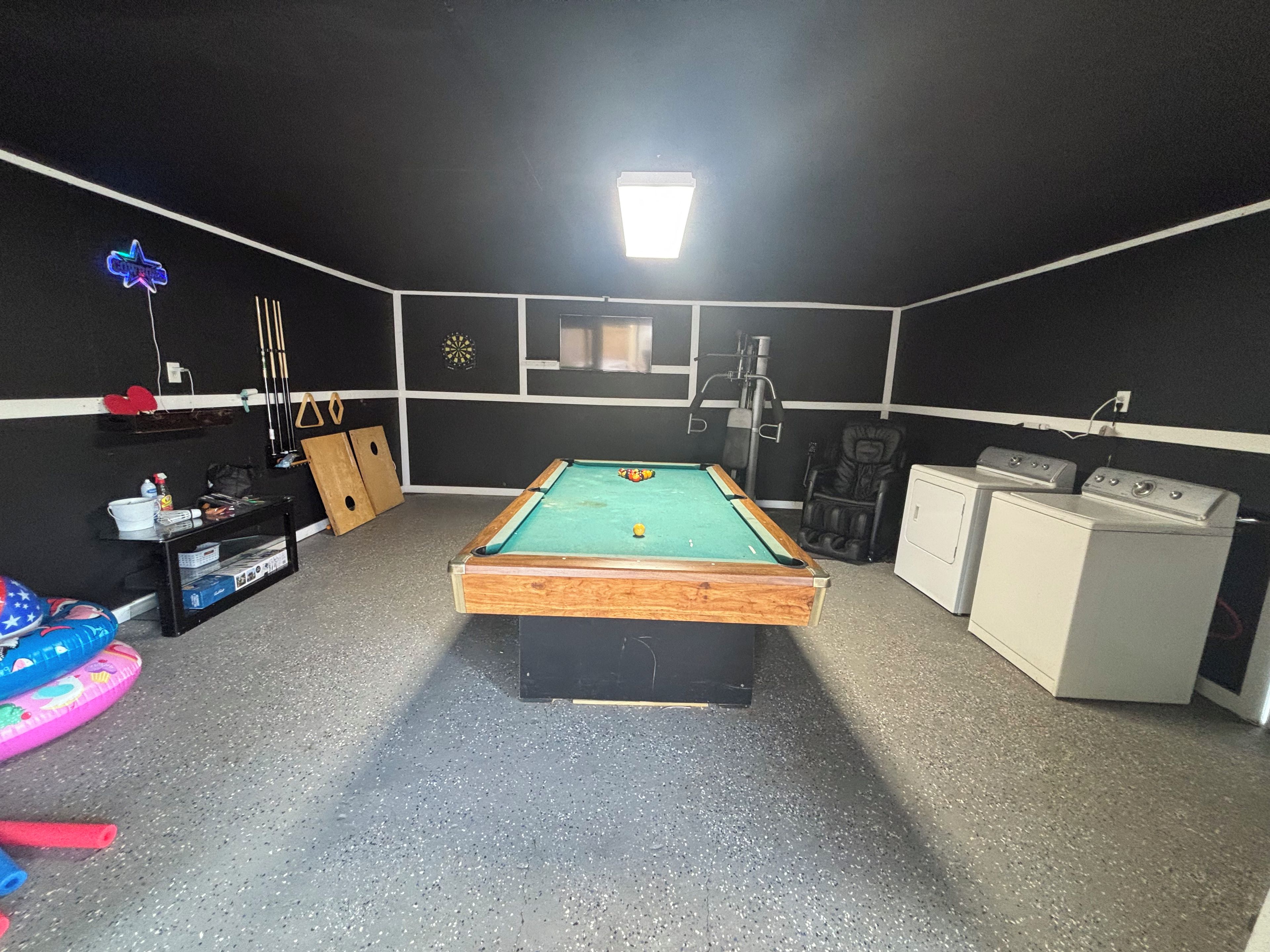 A pool table in a room with a black and white color scheme, a dartboard, and a massage chair.
