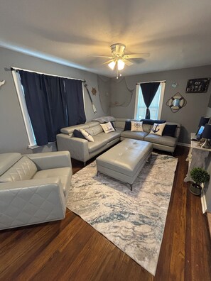 Ein Wohnzimmer mit einem Ecksofa, einer Liegesessel, einem Couchtisch und einem Deckenventilator.