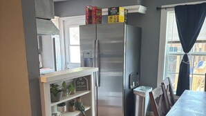 A kitchen with a stainless steel refrigerator, a wooden dining table, and a white cabinet with decorative items. -    Cozy Three bedroom, Family-Friendly Home with Pool, Game Room & Fast Wi-Fi (Corpus Christi)