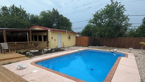 A rectangular swimming pool with a brick border, surrounded by a wooden deck and a concrete patio. -    Cozy Three bedroom, Family-Friendly Home with Pool, Game Room & Fast Wi-Fi (Corpus Christi)