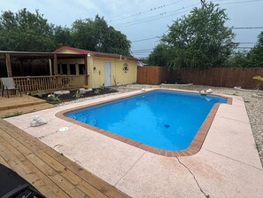 Ein rechteckiger Pool mit Ziegelsteinkante, umgeben von einer Holzterrasse und einer Betonplattform.