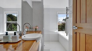 A modern bathroom with a wooden vanity, a large sink, and a glass shower enclosure. - Views on Devon West - New Plymouth (New Plymouth)