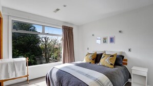 A bedroom with a large window, a bed with a striped blanket, and a small white nightstand. - Views on Devon West - New Plymouth (New Plymouth)