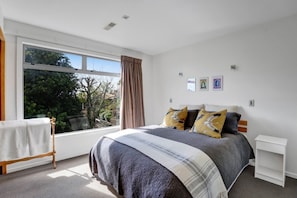 A bedroom with a large window, a bed with a striped blanket, and a small white nightstand. - Views on Devon West - New Plymouth (New Plymouth)