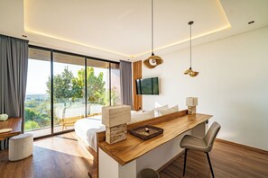 A modern bedroom with a large bed, a wooden desk, and a view of greenery outside. - Villa Sukha Senja Bingin (Pecatu)