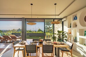 A dining area with a table set for four, surrounded by chairs, with a view of greenery outside. - Villa Sukha Senja Bingin (Pecatu)