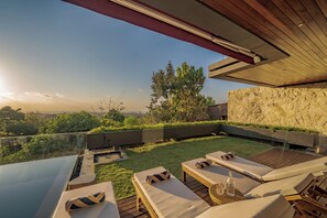 A modern outdoor lounge area with sun loungers, a pool, and a view of the landscape. - Villa Sukha Senja Bingin (Pecatu)