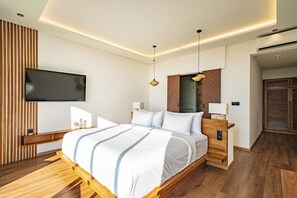 A modern bedroom with a wooden bed, a flat-screen TV mounted on the wall, and a wooden floor. - Villa Sukha Senja Bingin (Pecatu)