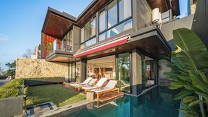 Ein modernes Haus mit Swimmingpool, Sitzgelegenheiten im Freien und einer Steinmauer.