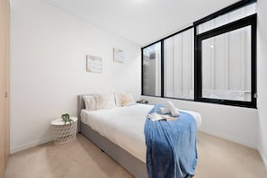 A bedroom with a bed, a window, a bedside table, and a small plant. - Sleek CBD Apartment | Steps to Everything Sydney (Sydney)