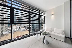 Een modern balkon met uitzicht op een stadsbeeld, een grijze stoel, een witte bank en een kleine tafel met een kopje en een plant.