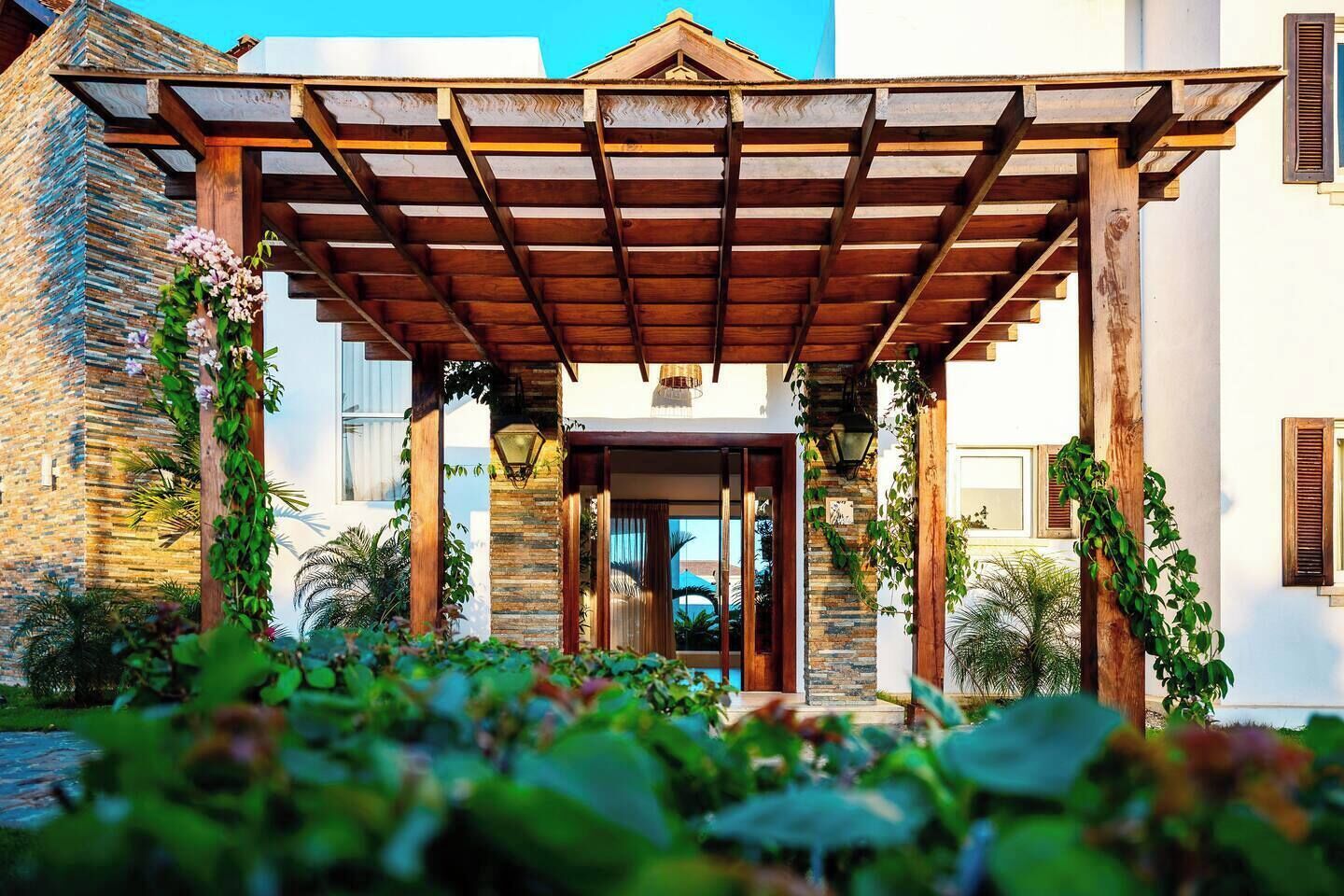 Un'area esterna riparata con una pergola in legno, pareti in pietra e vegetazione.