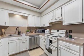 A modern kitchen with white cabinets, a stainless steel dishwasher, a microwave, a stove, and a coffee maker.