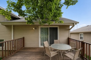 A covered patio with a table and chairs, a wooden deck, and a house with siding and a door.