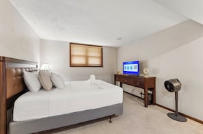 A bedroom with a bed, a television, a desk, and a standing fan.