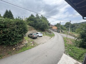 A rural road with two parked cars, surrounded by greenery and a house in the distance. - El Valle de la Reina House (Romillo)