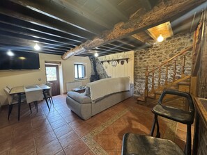 Ein rustikales Interieur mit Steinwand, einer Holztreppe, einer Couch, einem Esstisch und einem Fernseher.