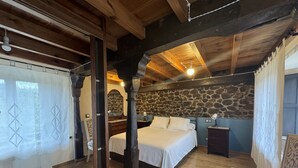 A bedroom with a stone wall, wooden beams, a bed, a chair, and a nightstand. - El Valle de la Reina House (Romillo)