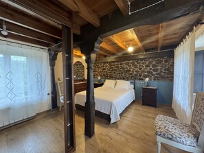 A bedroom with a stone wall, wooden beams, a bed, a chair, and a nightstand. - El Valle de la Reina House (Romillo)