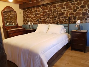 Ein Schlafzimmer mit Steinwand, einem Bett mit weißer Bettwäsche, einem Schminktisch, einem Nachttisch und einer Lampe.