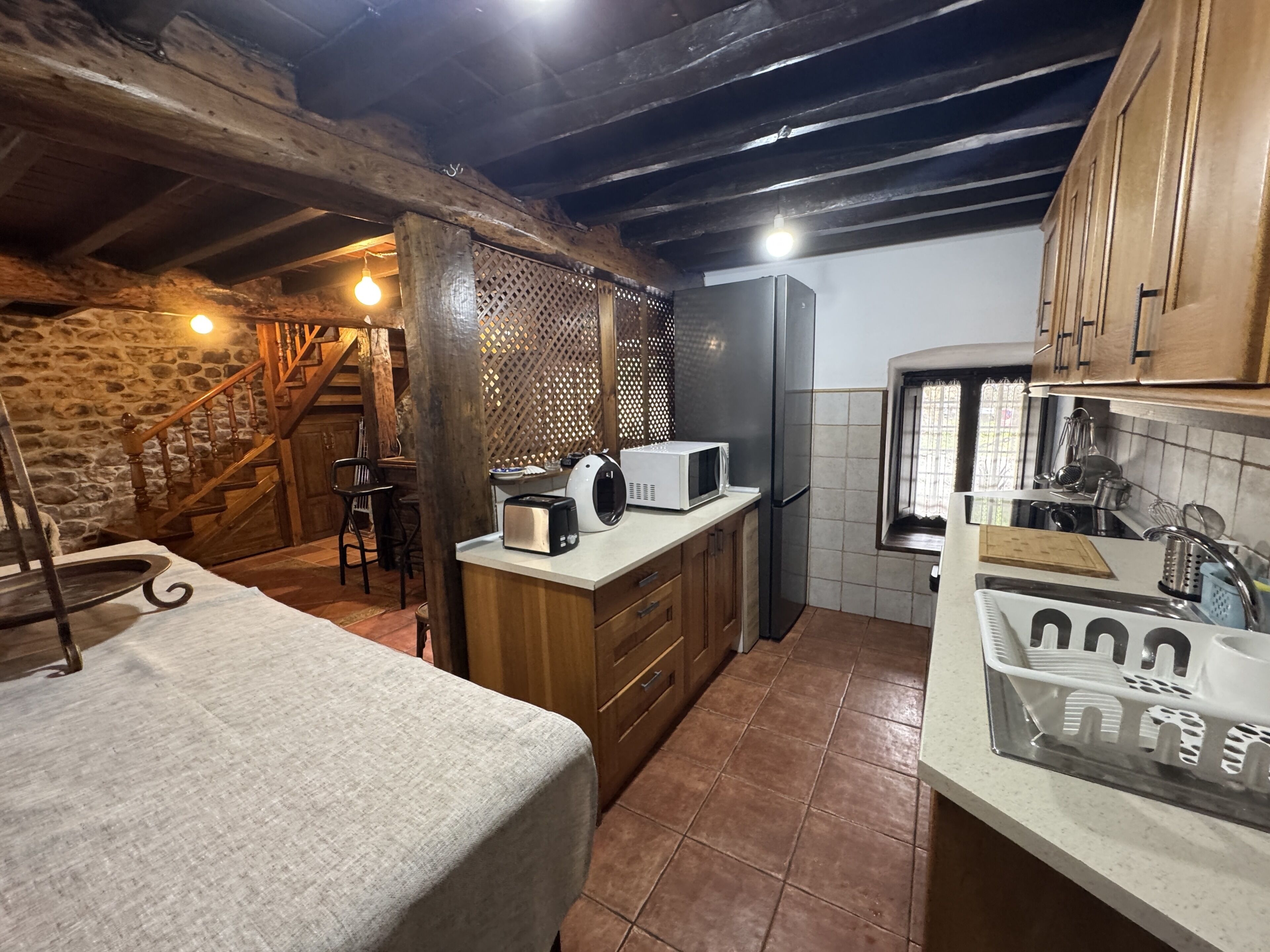 A rustic kitchen with wooden beams, a stone wall, and a wooden staircase.