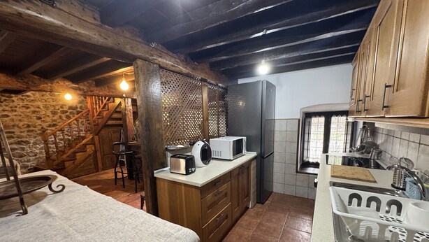 A rustic kitchen with wooden beams, a stone wall, and a wooden staircase. - El Valle de la Reina House (Romillo)